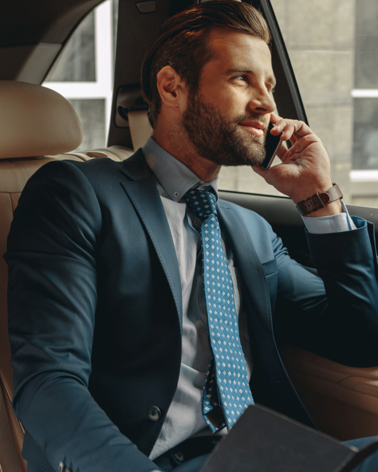 Business professional taking a phone call in a car with a laptop on their lap.