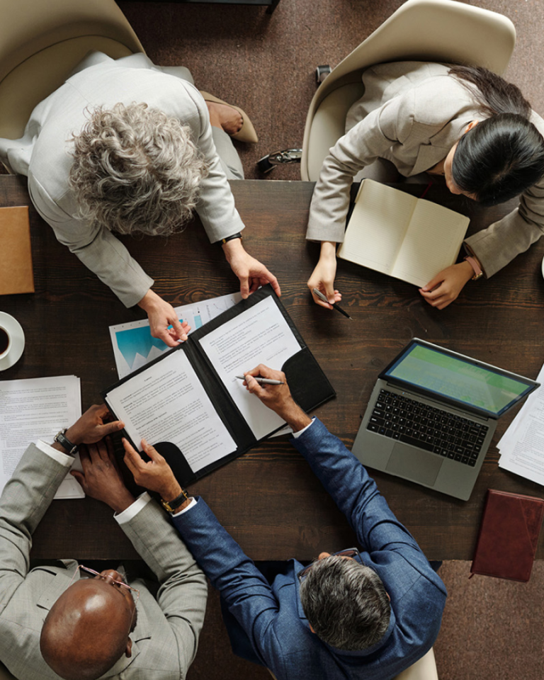 Aerial view of a team meeting with documents, reports, and a laptop spread across a conference table.