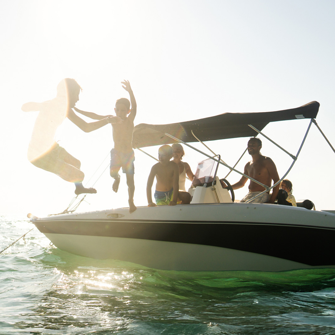 People having fun on a boat, with two individuals jumping into the water on a sunny day.