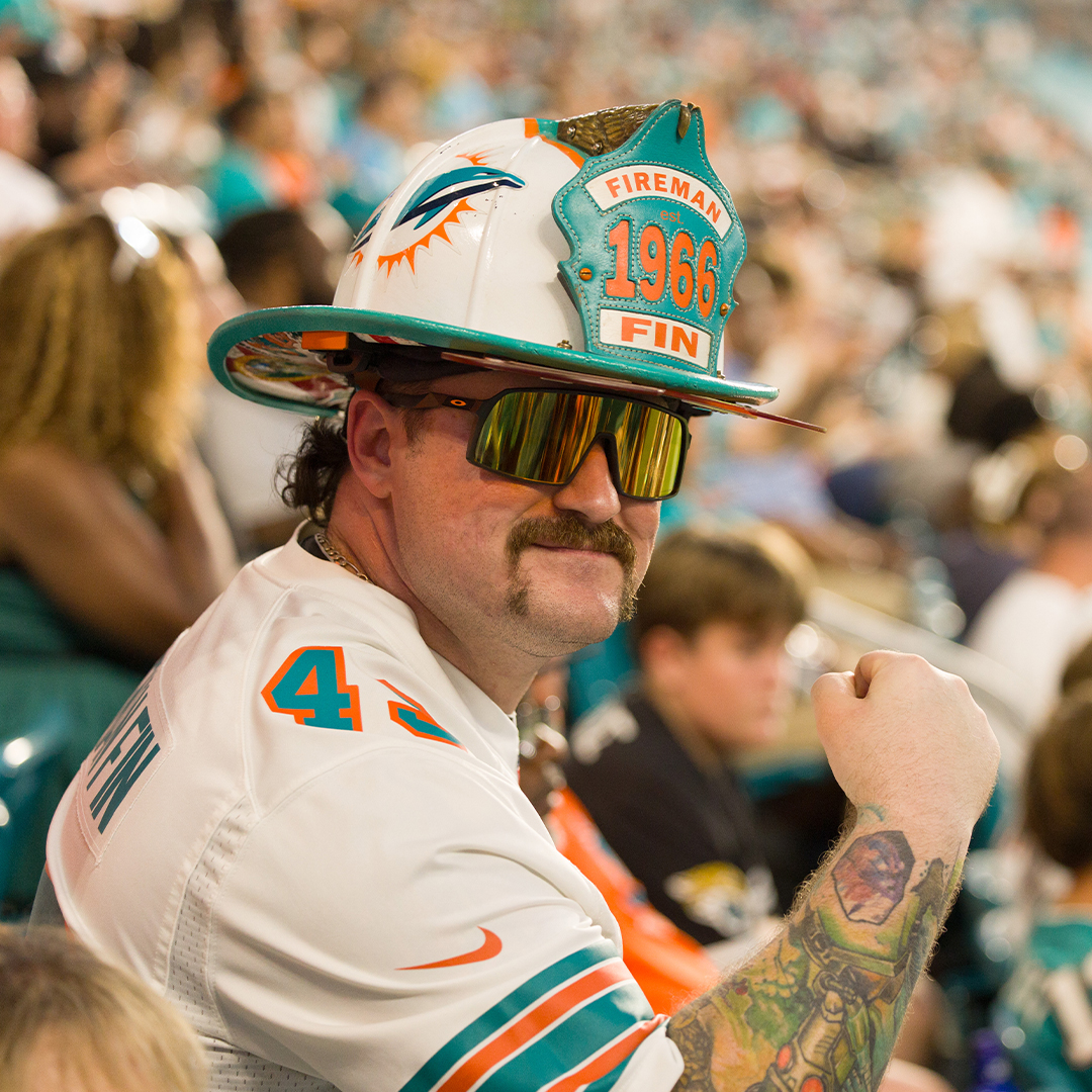 Miami Dolphins fan in firefighter hat motions towards the camera