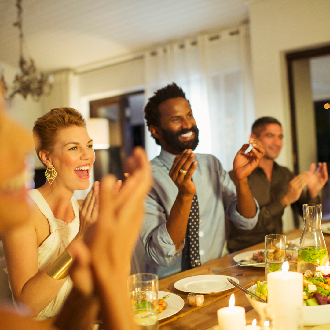 People gathered around a dining table, sharing a meal and applauding during an indoor celebration.