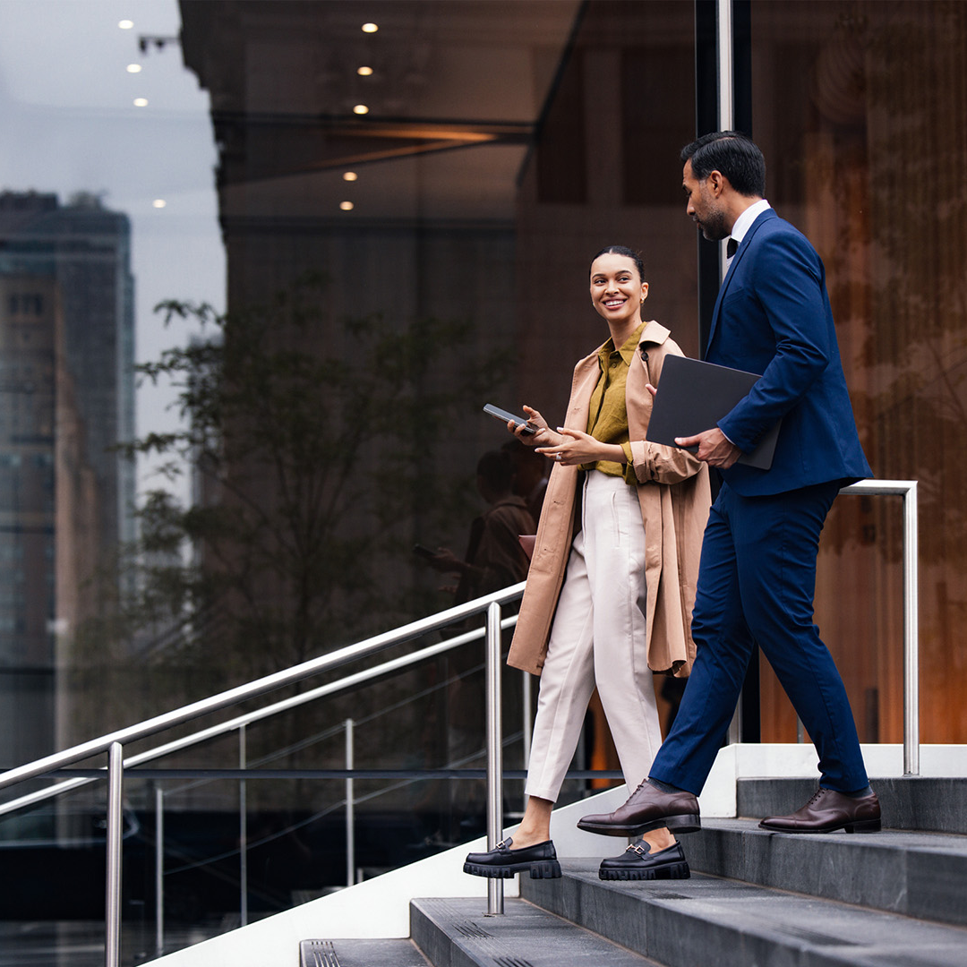 Two professionals walking down office building steps while discussing work.